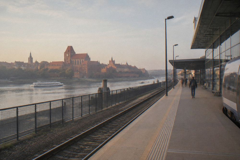 A railway platform beside a modern station building on the bank of the Vistula river