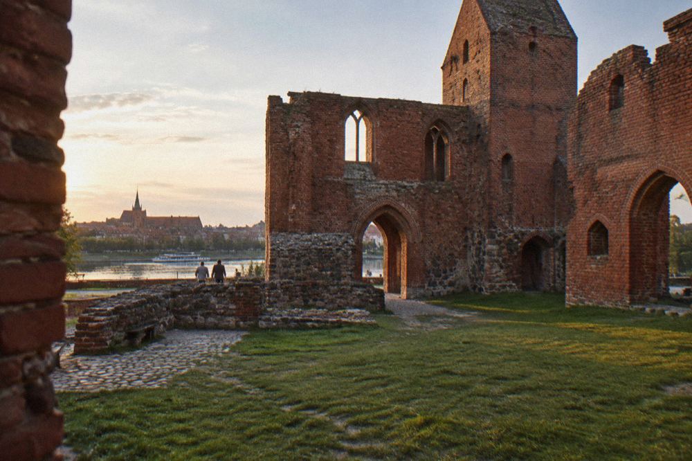 Red brick ruins of the Teutonic Castle with arched doorways and grass underfoot in Toruń