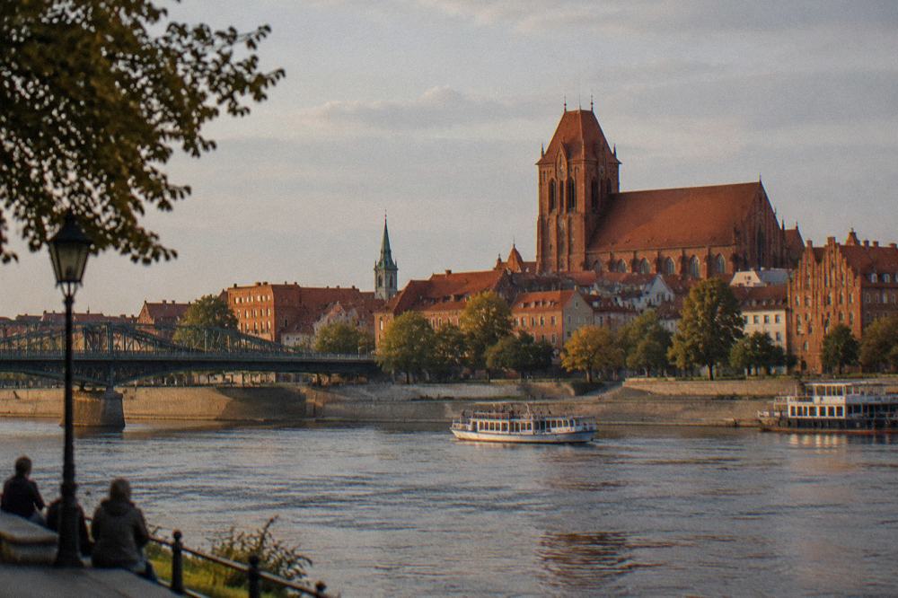 A red brick Gothic church tower seen across rooftops from the far bank of the Vistula river