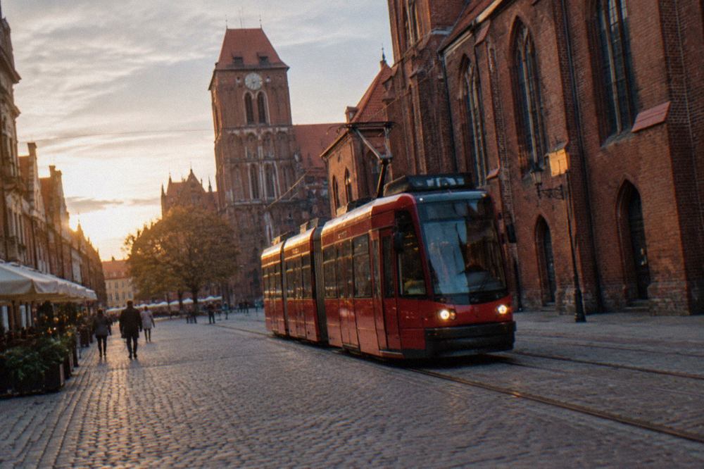 A red city tram moving along a street lined with brick Gothic buildings in Toruń