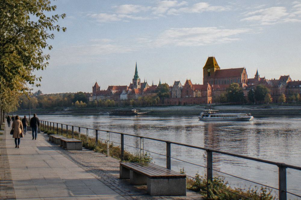 A riverside walkway beside the Vistula with the Toruń skyline of towers and spires behind