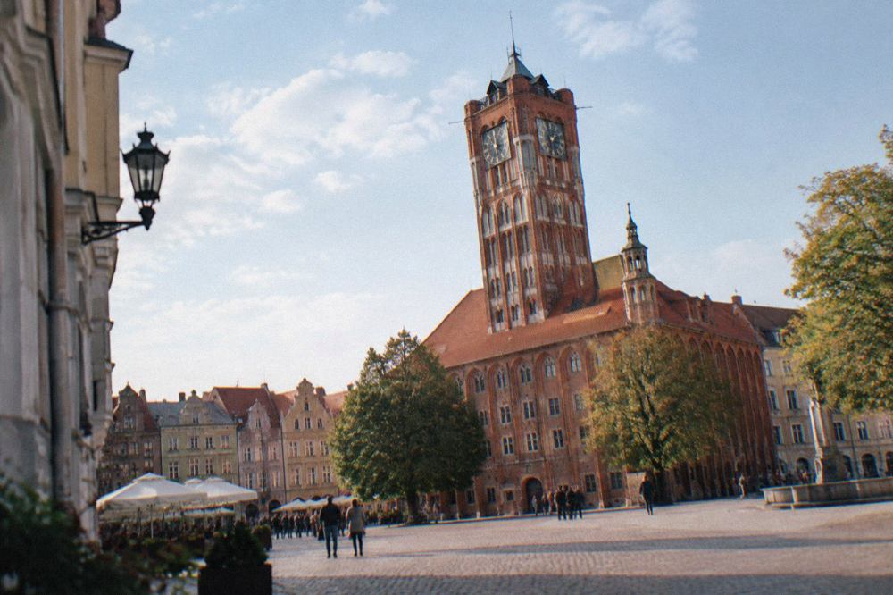 The red brick Old Town Hall tower rising above the rooftops of Toruń's market square on a bright day