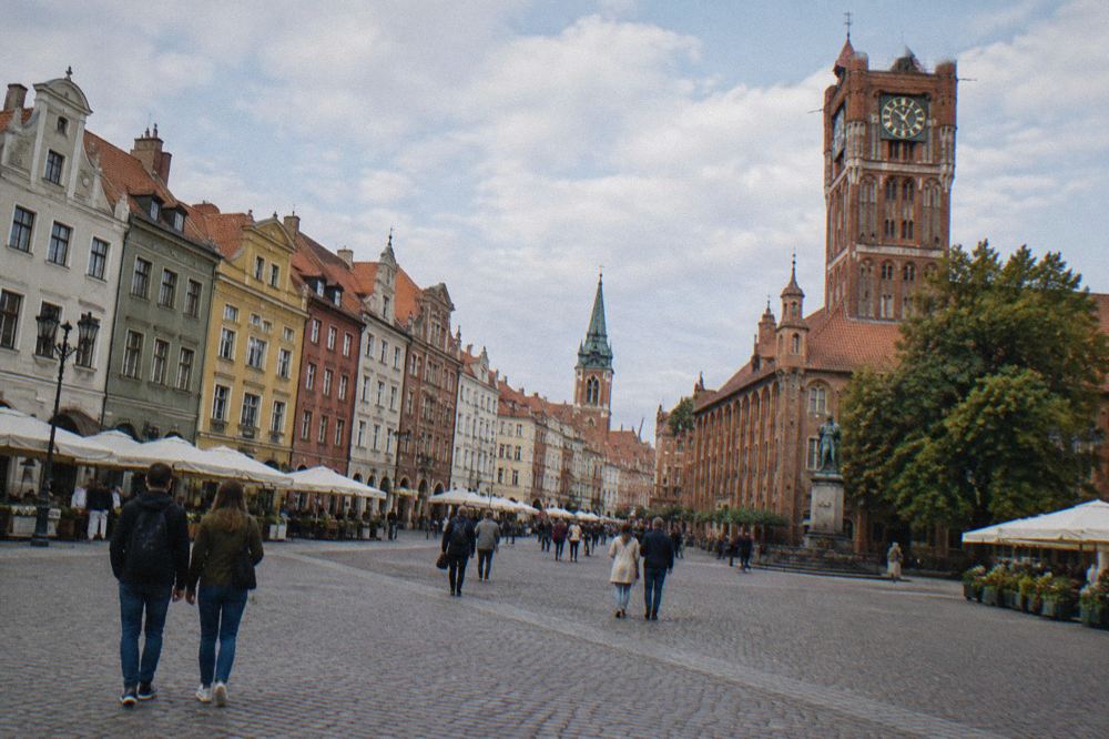 Visitors walking across the broad market square in Toruń's Old Town past coloured merchant houses
