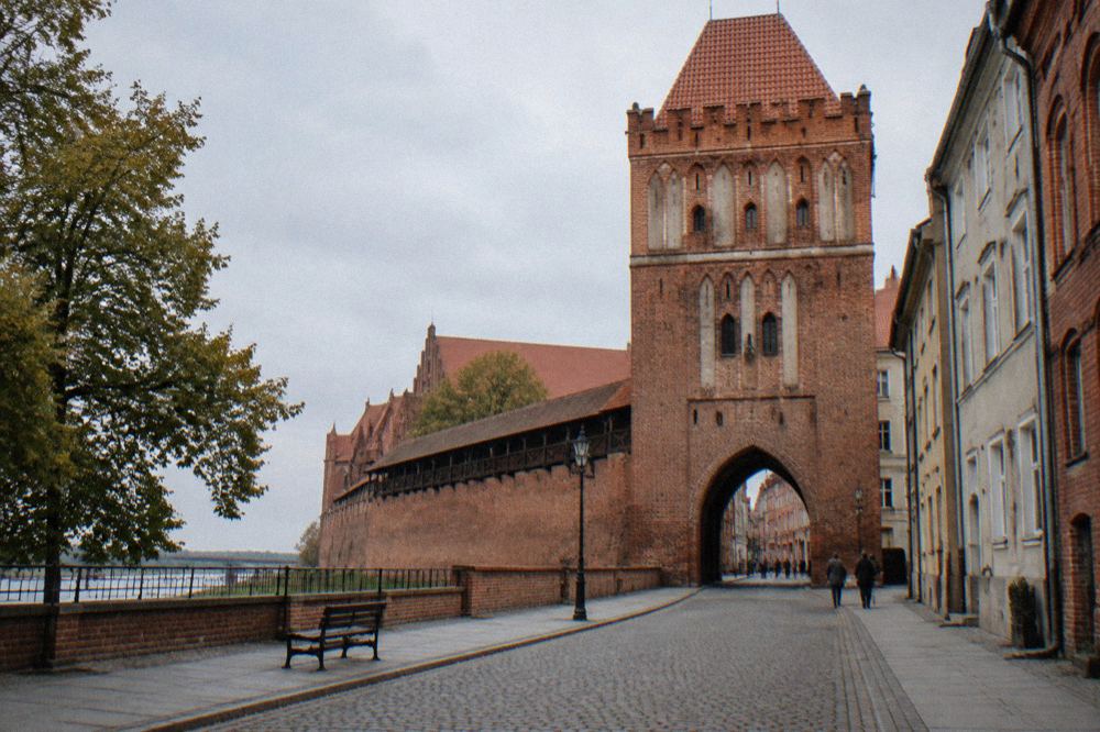 A Gothic brick gate tower in Toruń's medieval city wall seen from a quiet street