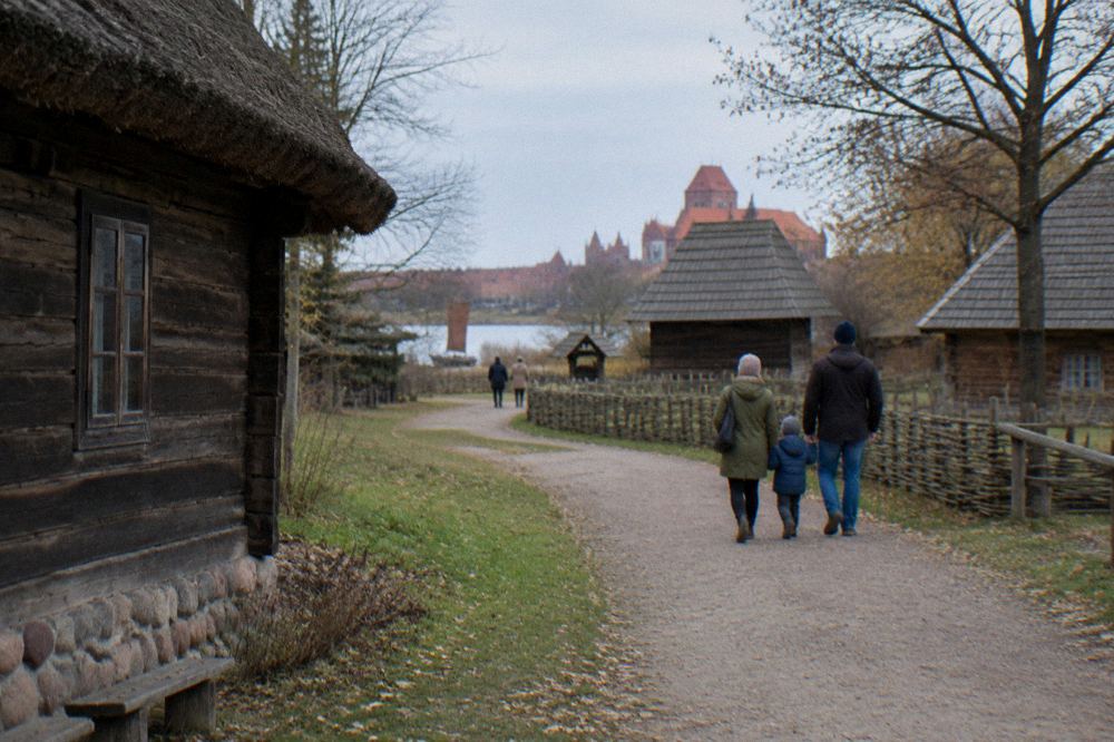 A family walking a path through the open-air Ethnographic Park with old wooden rural buildings