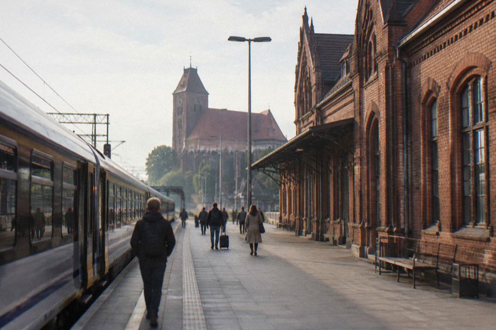 A passenger train standing at a platform beside a Polish railway station building