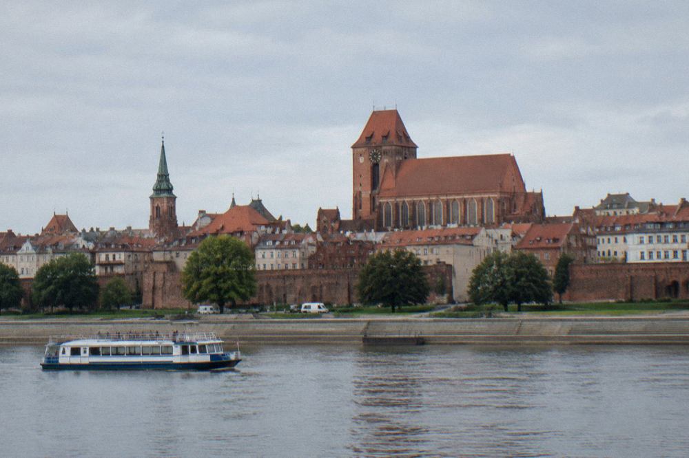 Panoramic view of the red brick towers and rooftops of the Old Town of Toruń seen from across the Vistula River