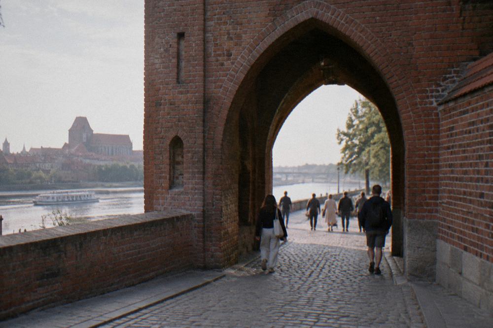 The arched brick gateway of one of the medieval Vistula side gates in Toruń with pedestrians passing through