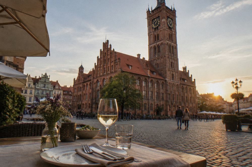 A table set for a meal on the Old Town Market Square in Toruń, with the town hall in view
