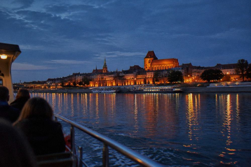 The illuminated outline of Toruń old town seen from a boat on the Vistula at dusk