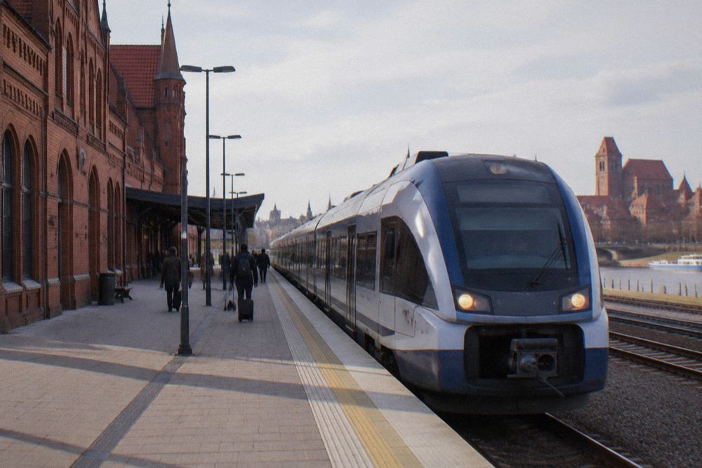 A modern train waiting at a platform beside a station building in Poland