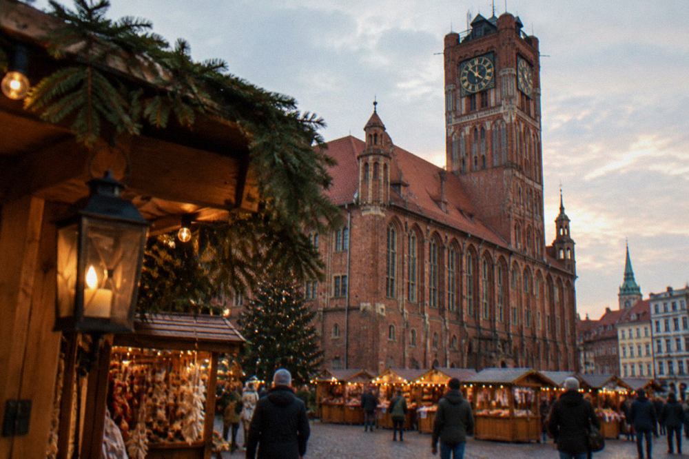 Wooden market stalls with glowing lights standing on a medieval square in front of a red brick town hall