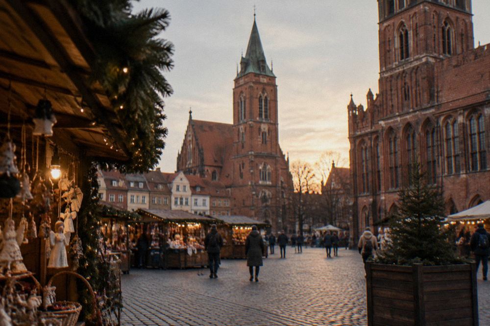 Festive stalls along the edge of a wide cobblestone square with gothic brick church towers behind