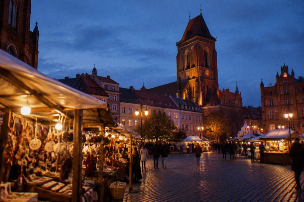 Evening view of illuminated market stalls with a gothic tower rising above the rooftops