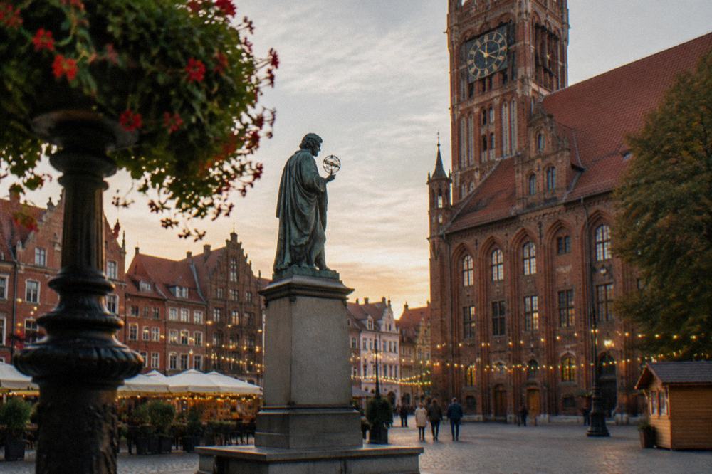 A monument statue on a square with brick townhouses and market lights strung between buildings
