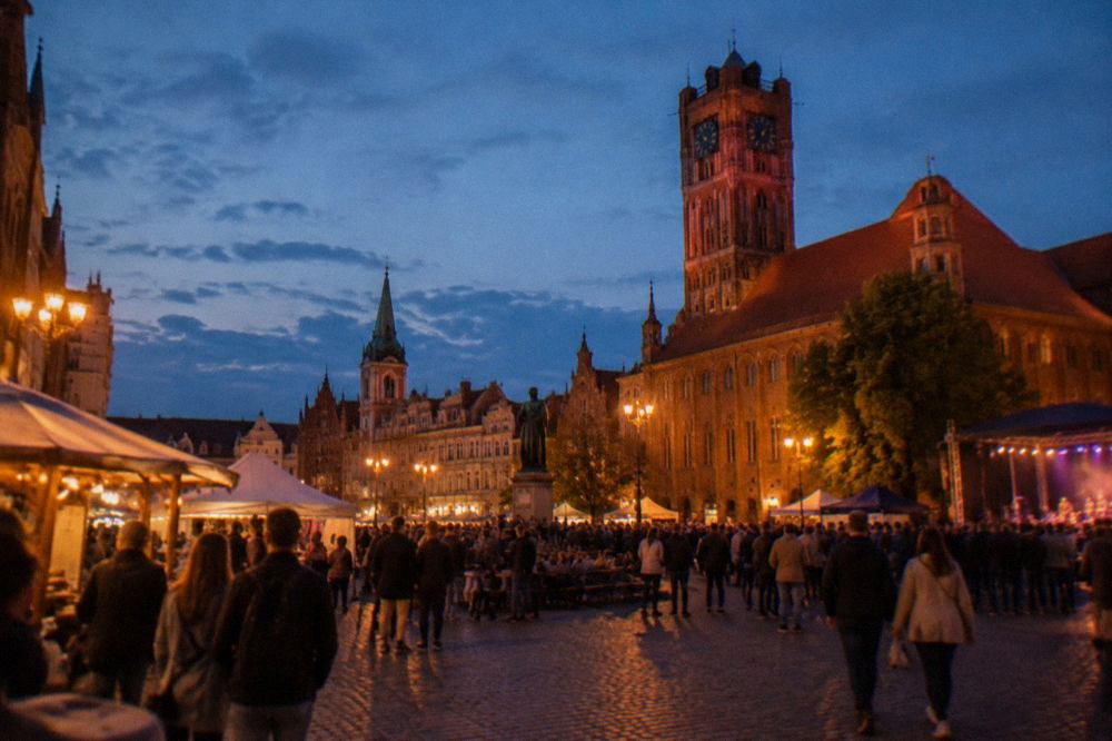 Crowds gathered in a lit medieval market square in Toruń during an evening festival
