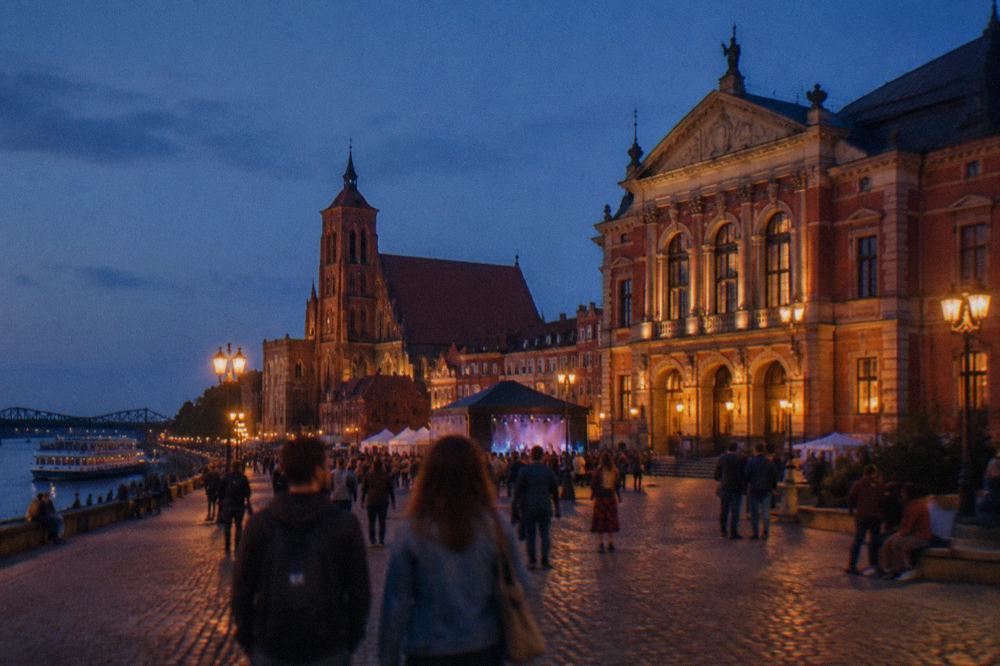 A historic theatre facade and festival-goers on an evening street in Toruń