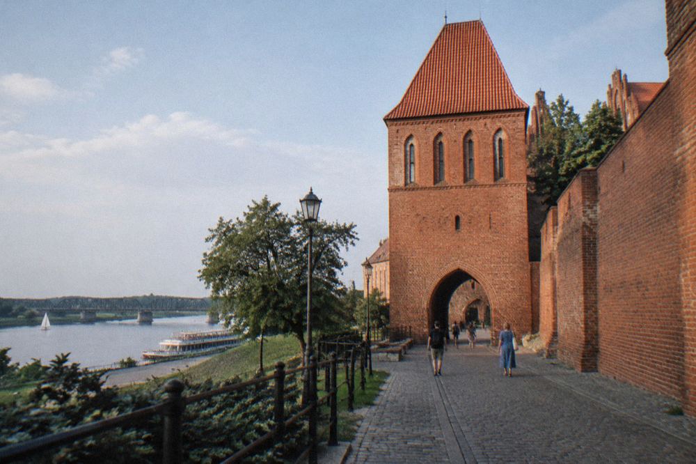 A stretch of red brick medieval wall with an arched gate tower under a blue sky