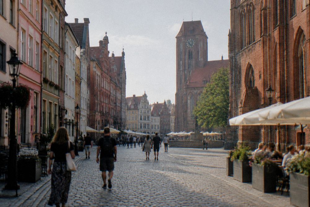 Visitors walking along a cobbled street between colourful medieval townhouses in Toruń