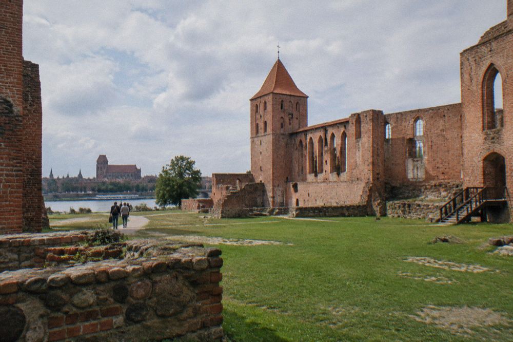 Red brick ruins of the Teutonic castle in Toruń seen across a grassy courtyard