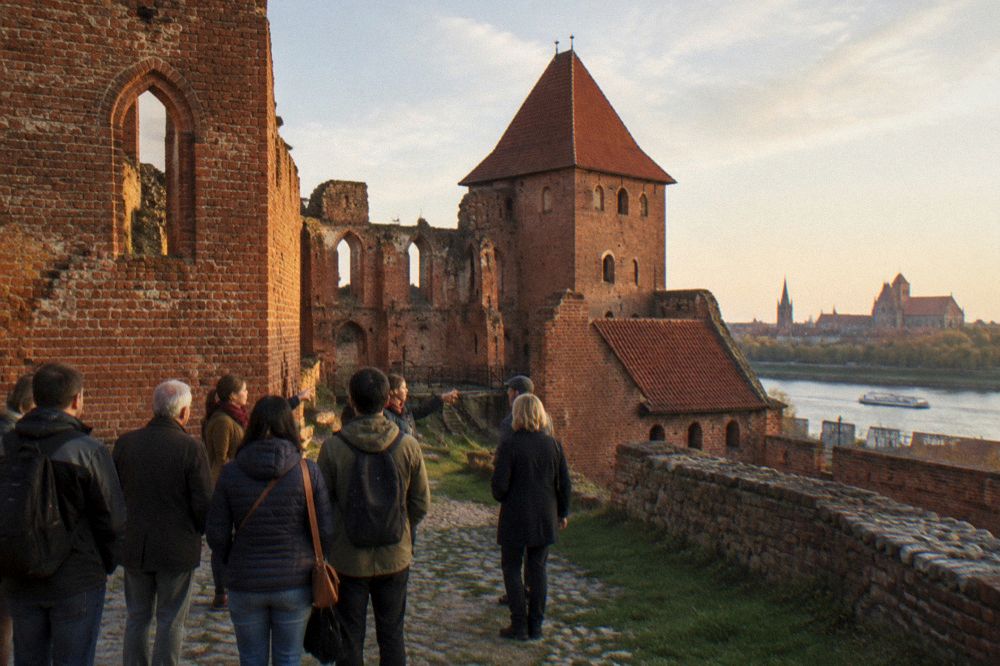 A guided walking group standing among red brick medieval buildings in Toruń