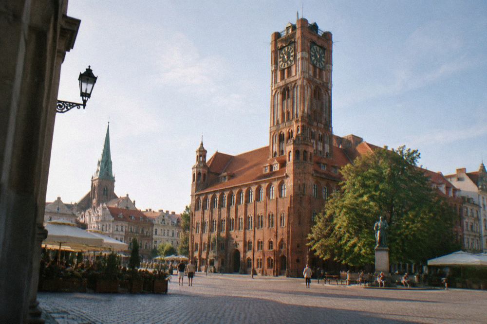 Gothic brick town hall tower rising above the old market square of Toruń on a bright day
