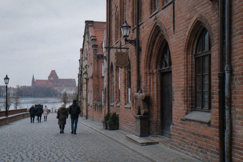 Visitors walking along a cobbled street of Gothic brick townhouses in Toruń's old town