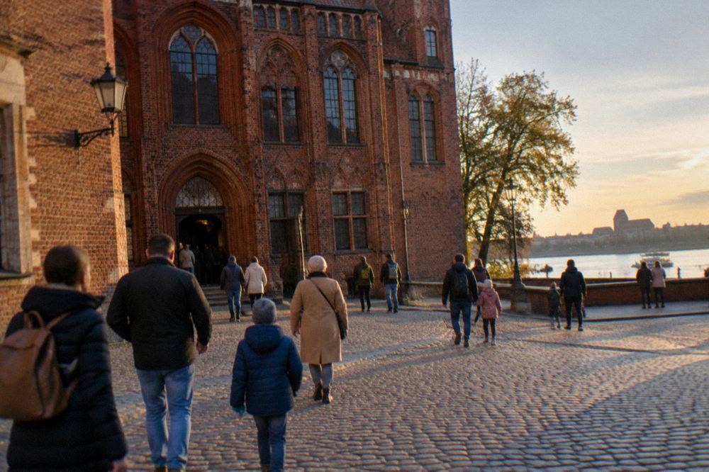 Families and visitors crossing an old town square towards museum entrances in Toruń