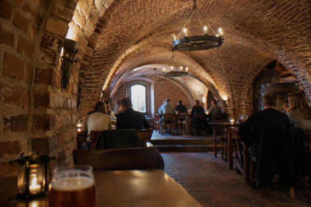 People seated at tables inside a brick-vaulted beer cellar under a brewery pub in Toruń
