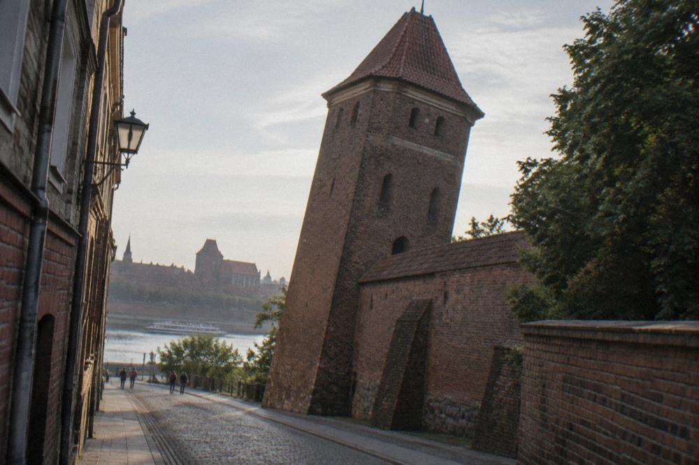 A narrow street in Torun with a leaning medieval brick tower standing in the old town wall