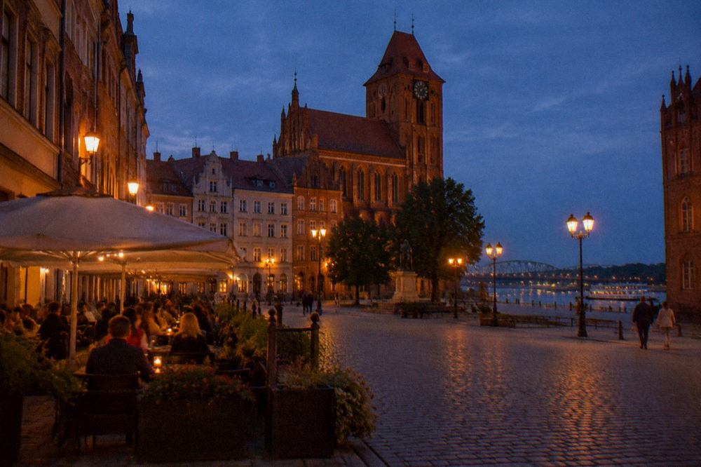 Evening diners seated at an outdoor table beside a historic townhouse in Toruń