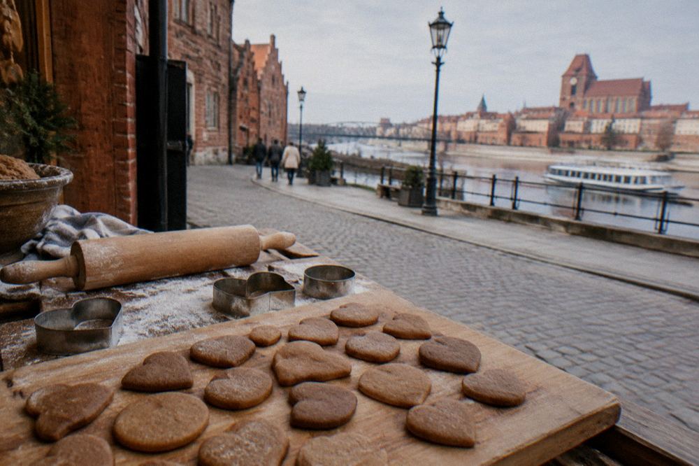 A wooden board of round and heart-shaped gingerbread cookies without any writing, a rolling pin and cutters beside, a Toruń bakery table.