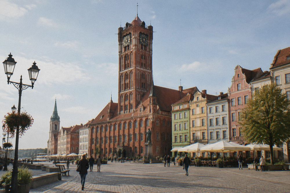 Gothic brick town hall tower rising above the coloured townhouses of the Old Town market square in Toruń