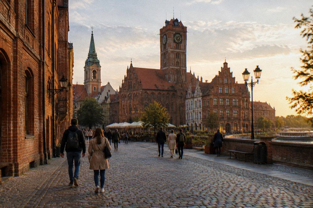 Visitors walking a cobbled medieval street lined with gothic brick townhouses in Toruń
