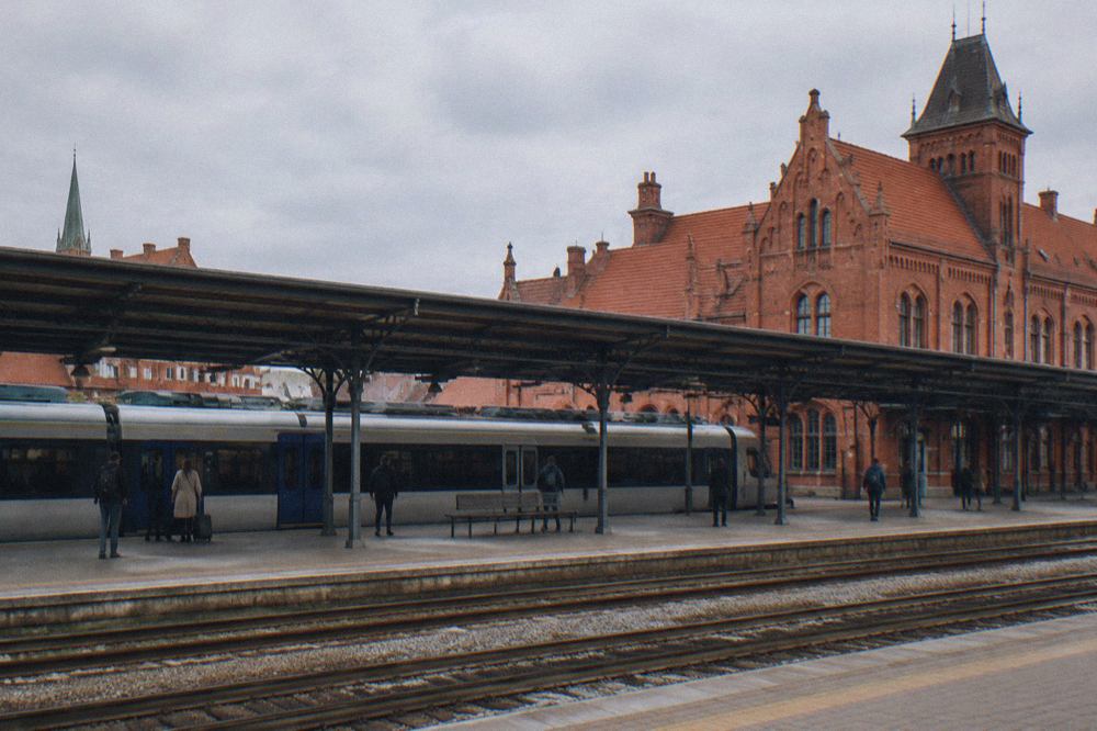 A railway station platform in Toruń with a passenger train stopped beside the sheltered walkway