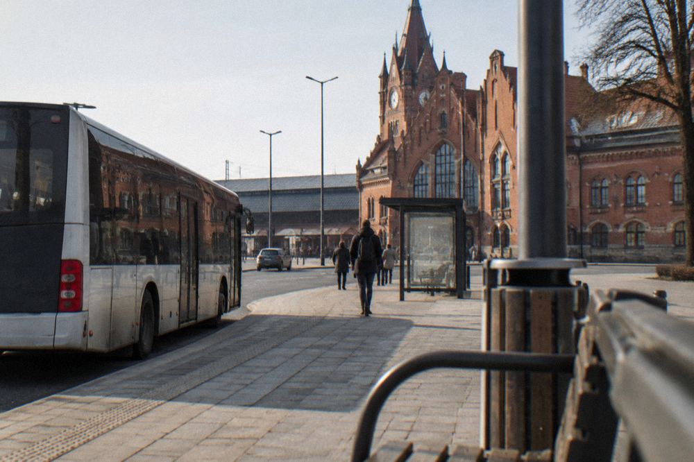 A city bus waiting at a stop near a railway station entrance in Toruń