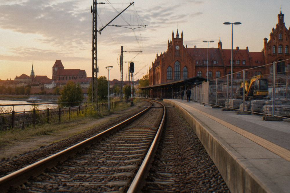 A railway line running toward a station building with construction fencing visible nearby