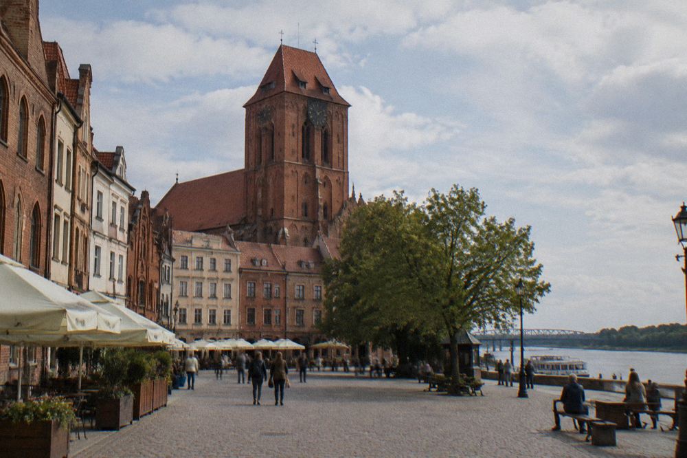 Red-brick Gothic church tower rising above Toruń old town street