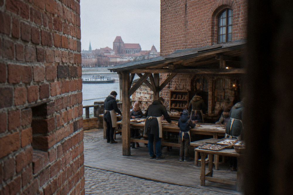 Visitors baking gingerbread at a wooden workbench in a museum show