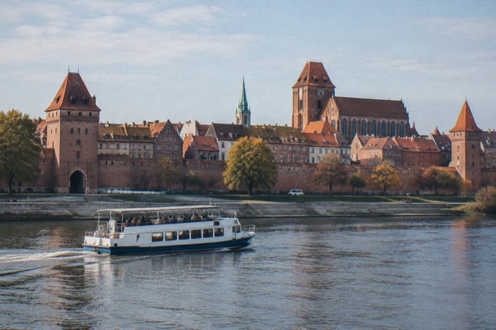 A passenger boat on the Vistula river passing the red brick walls and towers of Torun Old Town