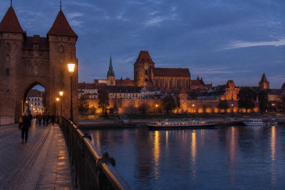 Red brick gothic church towers and town walls rising above the Vistula river in Torun at dusk