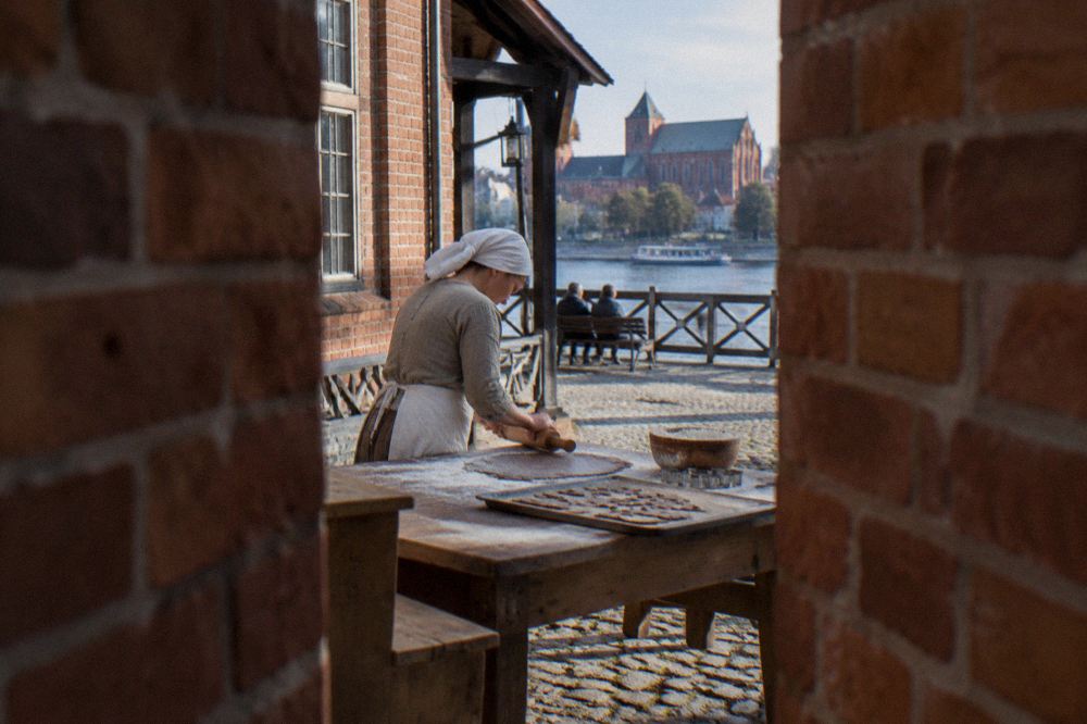 A baker in an apron rolling gingerbread dough on a floured wooden table