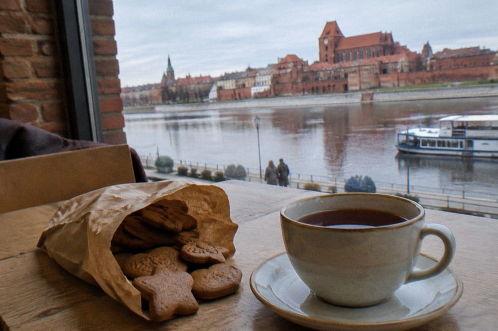 A paper bag of gingerbread biscuits resting beside a cup of tea on a cafe table