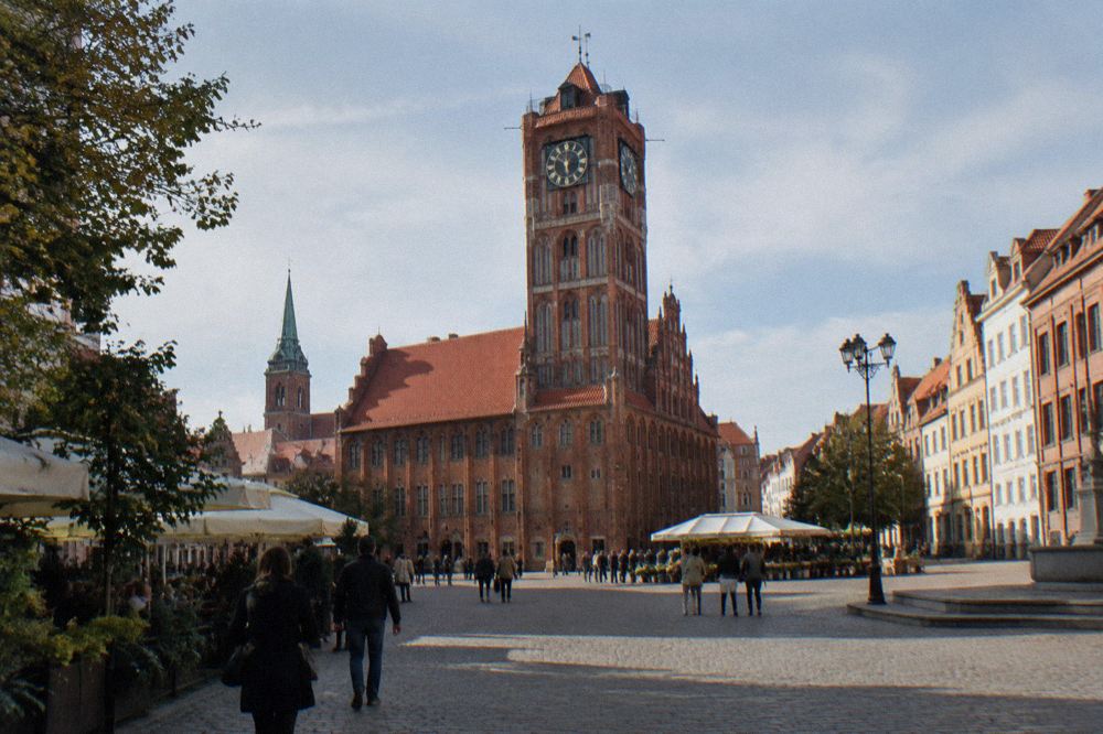 The Gothic brick Old Town Hall tower rising above red rooftops of Toruń market square
