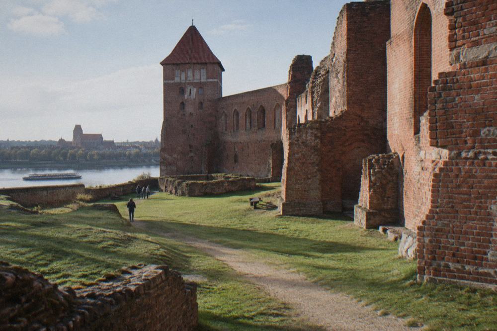Red brick ruins of the Teutonic castle in Toruń with grassy courtyard and footpath