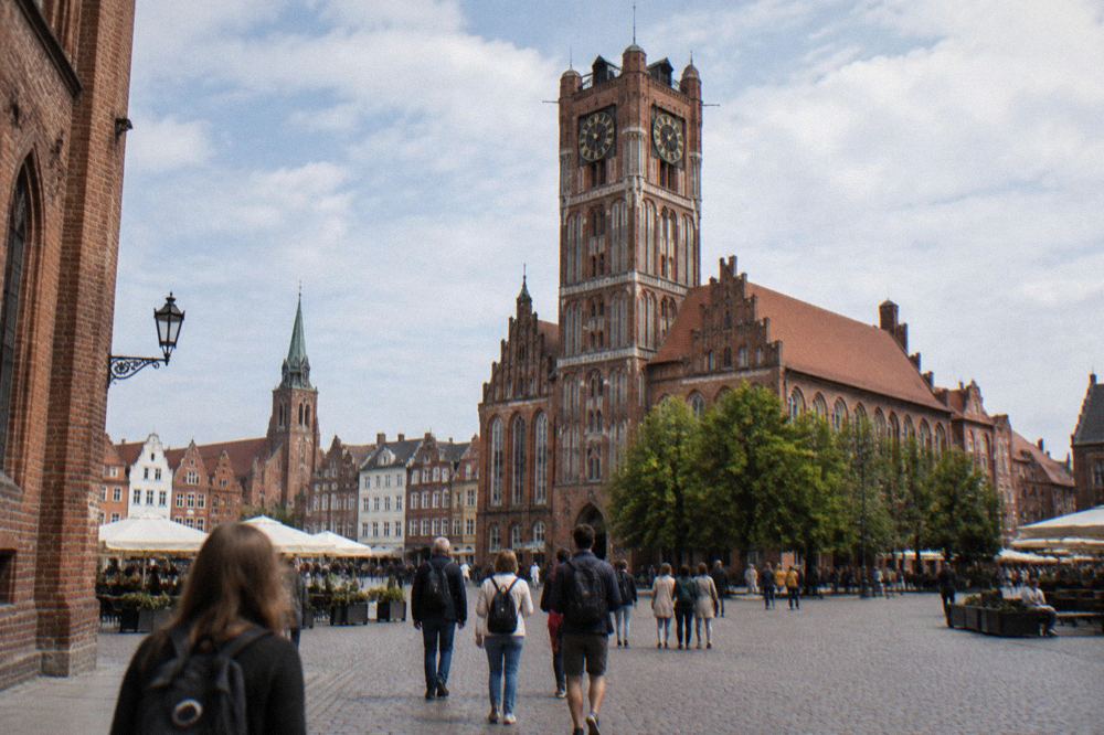 Tourists crossing the market square in Torun toward the brick Old Town Hall tower