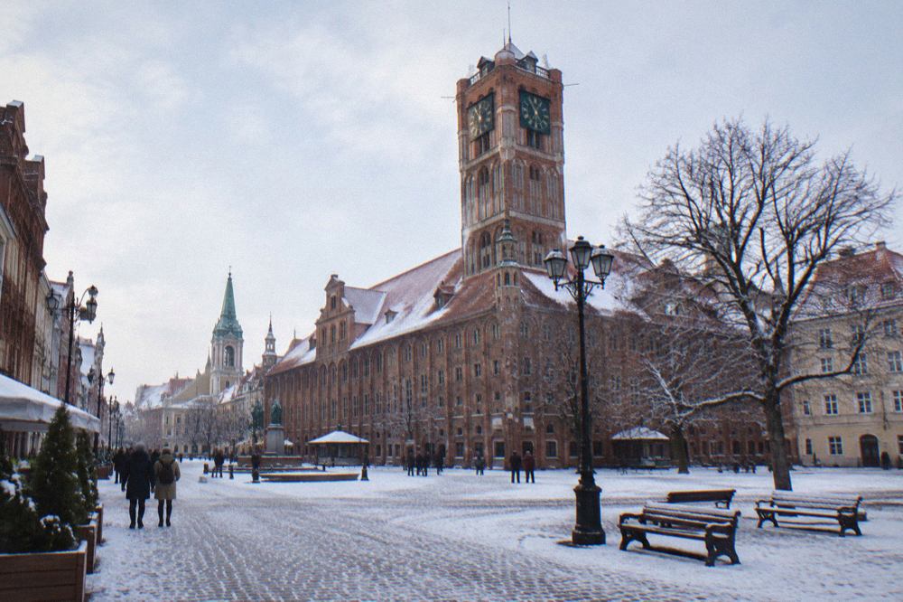 Snow-covered Old Town square in Toruń with the Gothic town hall tower rising above red rooftops