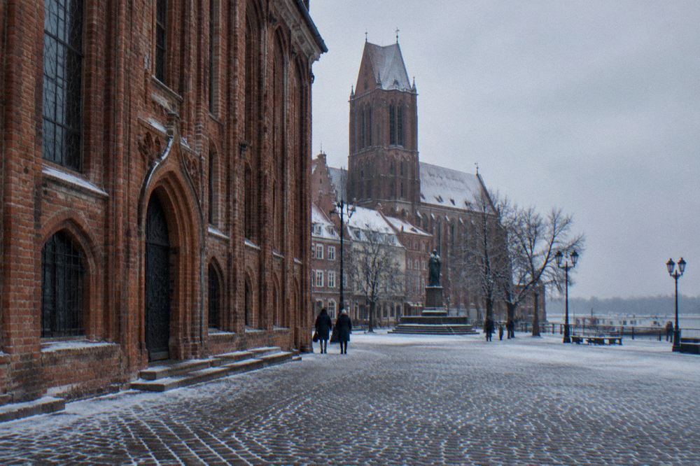 Frost-covered Gothic brick facade and cobbled street in Toruń under a grey winter sky