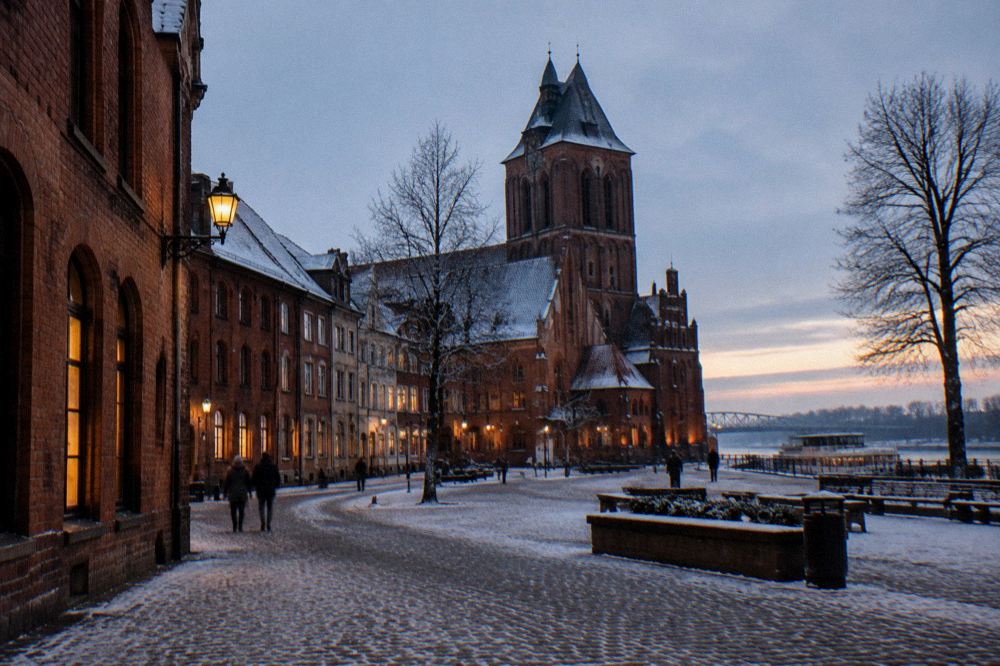 A quiet winter street in Toruń at dusk with lit windows and a Gothic tower in the background
