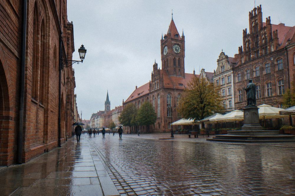 Rain-wet cobblestone street in the Old Town of Toruń with Gothic brick townhouses on both sides